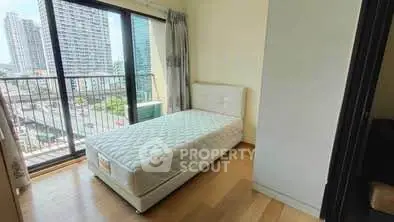 Cozy bedroom with single bed and city view from balcony in modern apartment.
