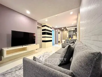 Modern living room with sleek design and large TV, open to dining area.