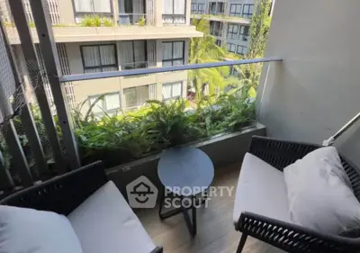 Charming balcony with cozy seating and lush greenery overlooking modern apartment complex.