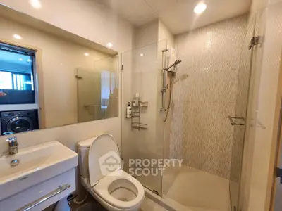 Modern bathroom with glass shower and washing machine in sleek apartment.