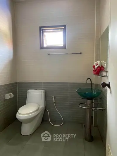 Modern bathroom with sleek design and glass sink, featuring a compact layout and natural light.