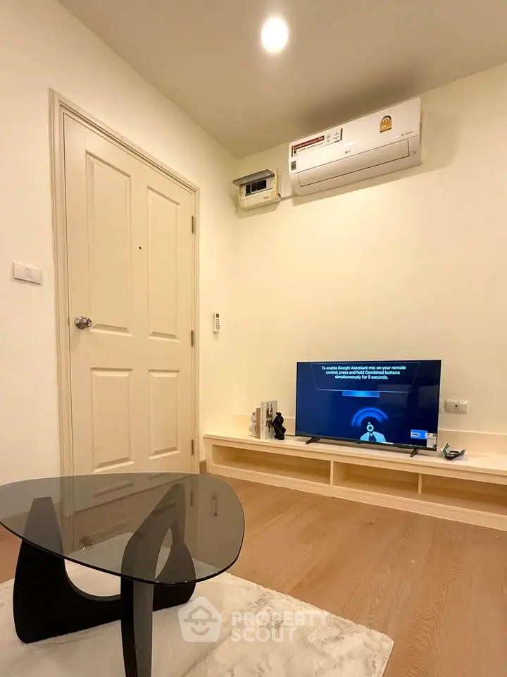 Modern living room with sleek glass table and wall-mounted TV under air conditioning unit.