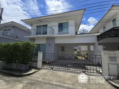 Modern two-story house with balcony and gated driveway in a suburban neighborhood.