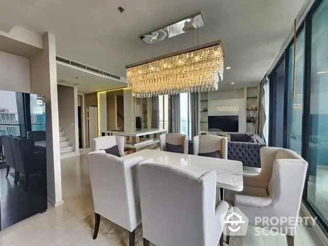 Luxurious open-plan living space with elegant dining set, chic chandelier, and expansive windows offering ample natural light.