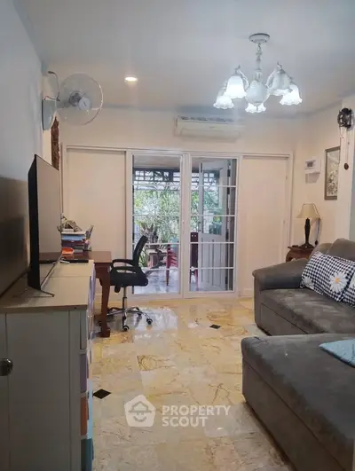 Cozy living room with marble flooring and sliding glass doors leading to a lush garden view.
