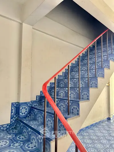 Stylish staircase with vibrant blue patterned tiles and red railing in modern building.