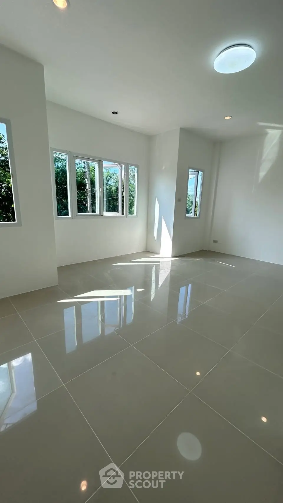 Spacious sunlit room with glossy tiled floors and large windows offering lush green views.