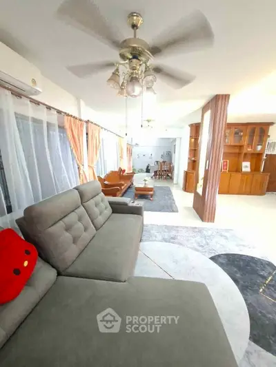 Spacious living room with modern furniture and ceiling fan, featuring large windows and elegant decor.
