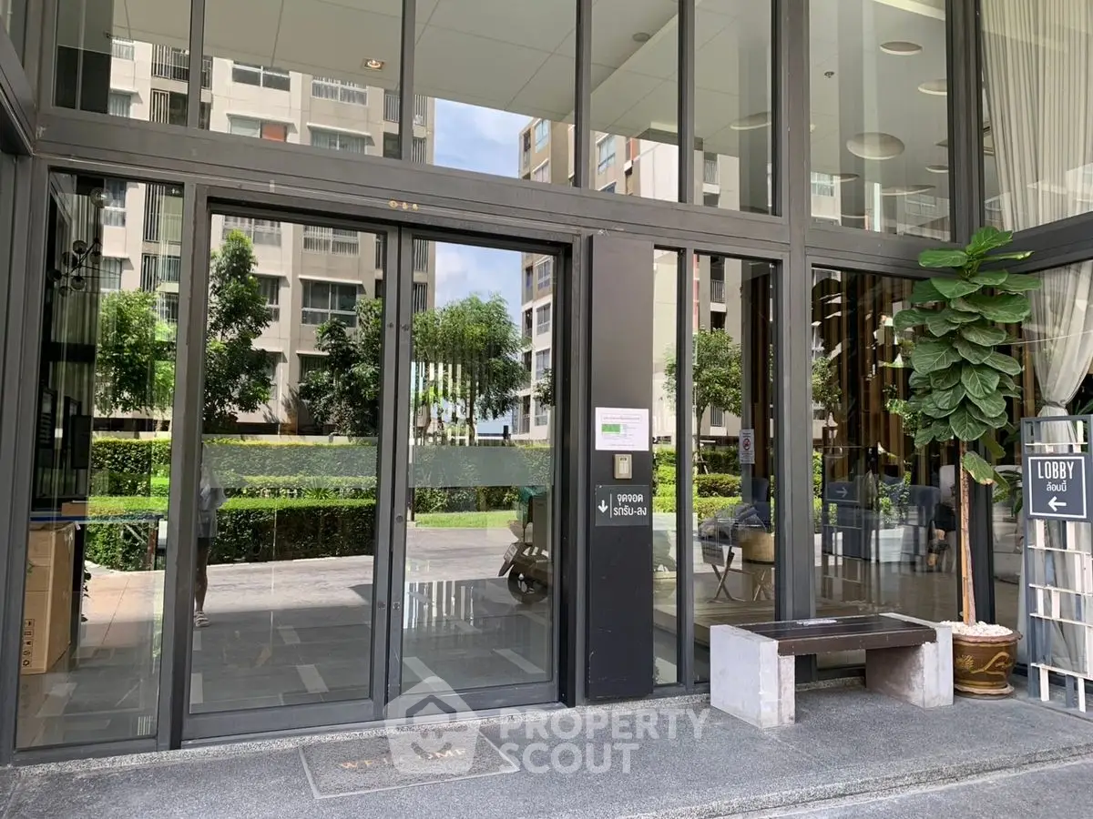 Modern building entrance with glass doors and lush greenery, inviting ambiance for residents and guests.