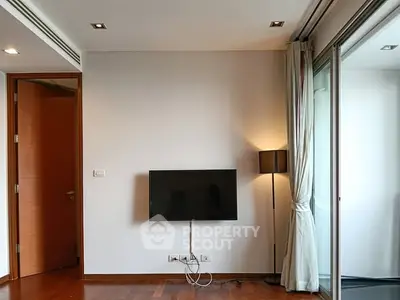 Modern living room with wall-mounted TV and floor lamp, featuring wooden flooring and sliding glass doors.
