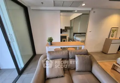 Modern living room with sleek furniture and glass doors leading to a balcony, showcasing a cozy and stylish interior.