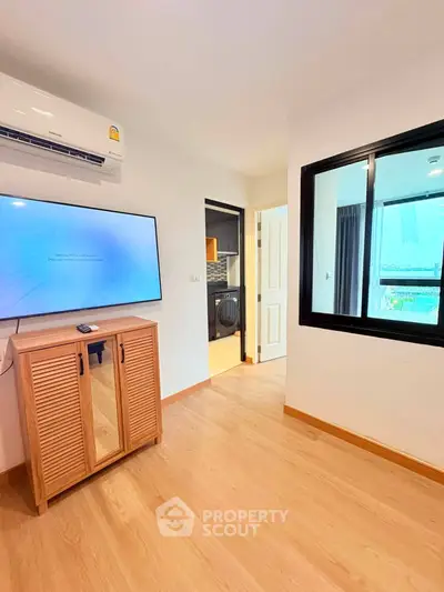 Modern apartment interior with wooden flooring, wall-mounted TV, and air conditioning unit.