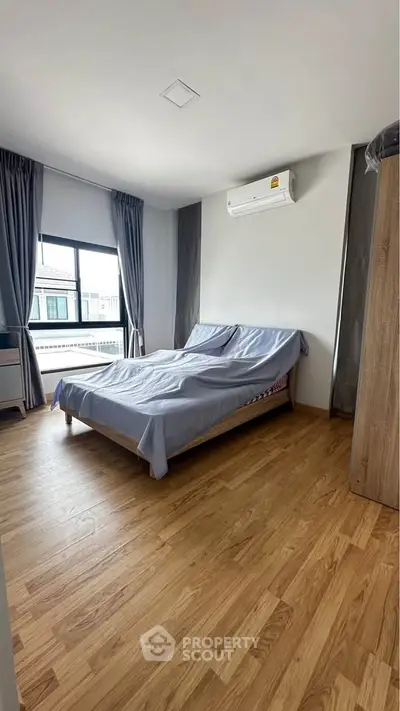 Spacious bedroom with wooden flooring and modern air conditioning unit.