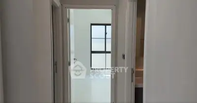 Bright hallway leading to a sunlit room with large window, showcasing modern minimalist design.