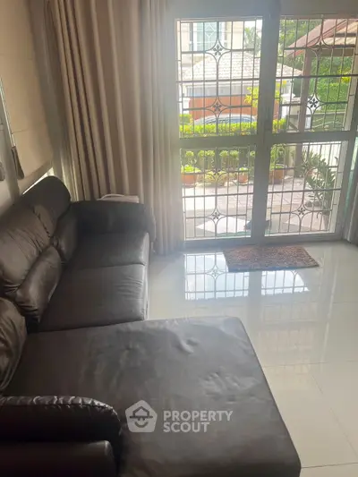 Cozy living room with leather sofa and garden view through large windows.