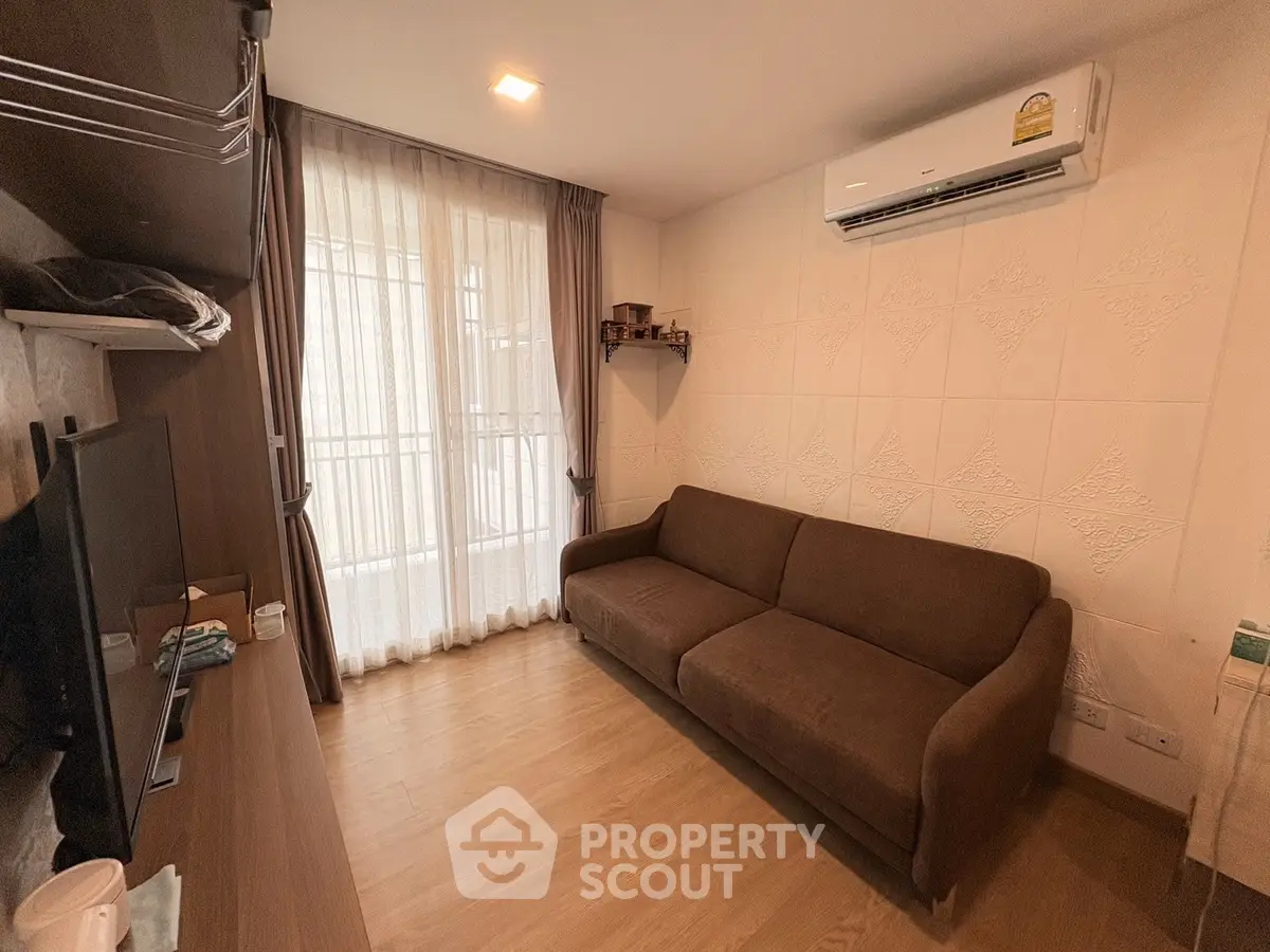 Cozy living room with brown sofa, wall-mounted TV, and air conditioning, featuring a balcony view.