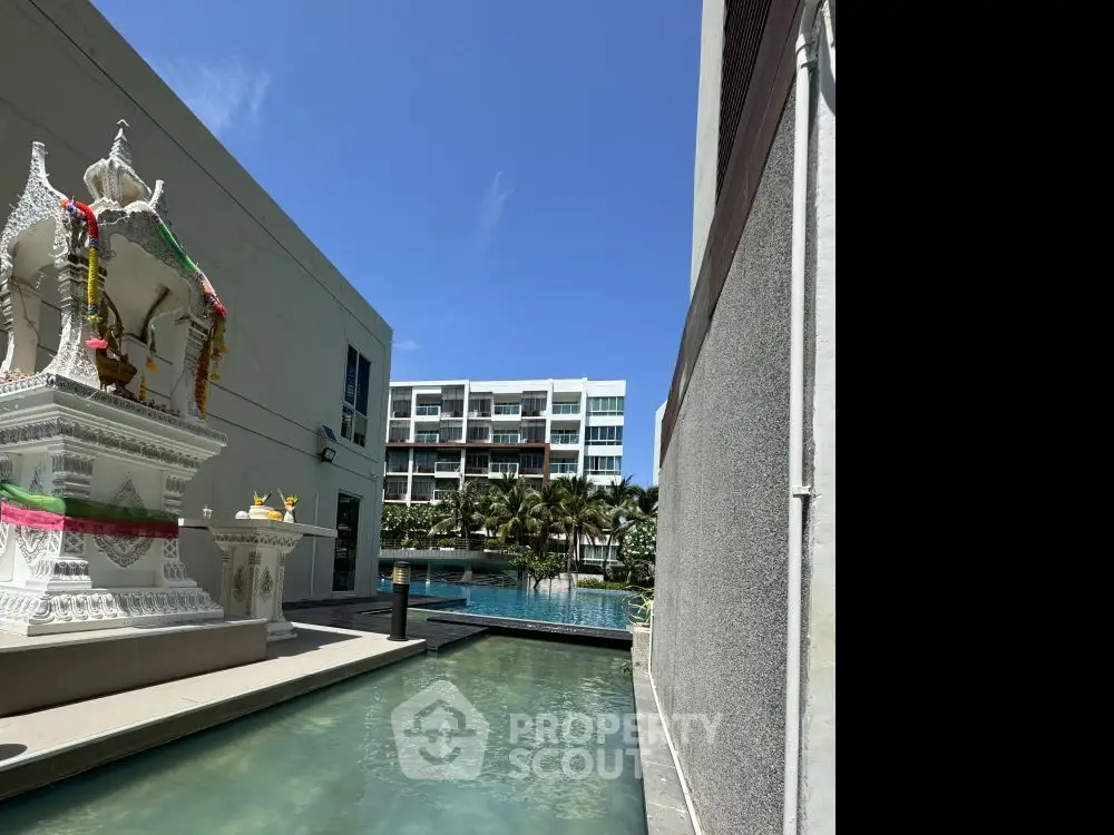 Modern apartment complex with pool and decorative statue under clear blue sky.