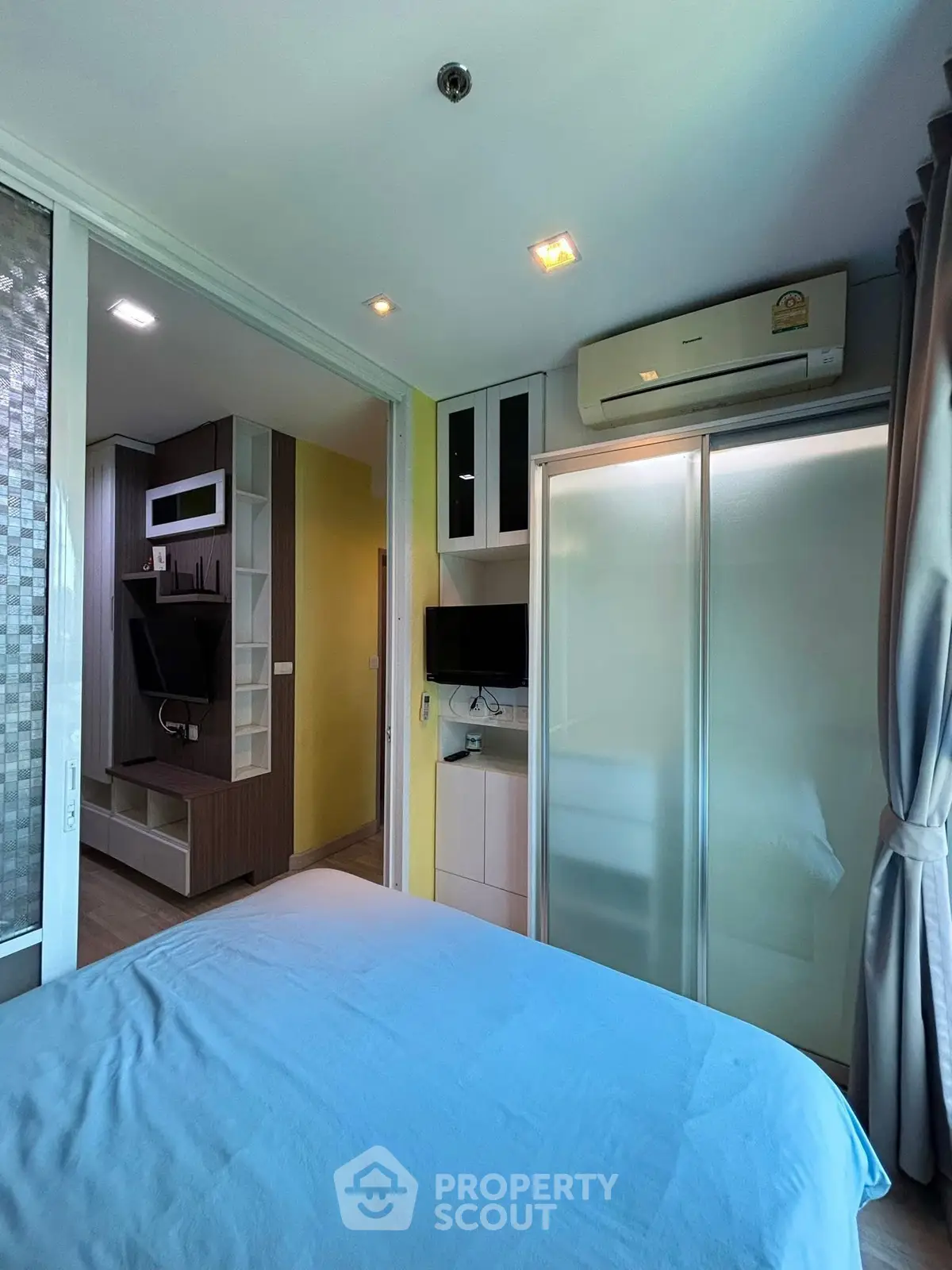 Modern bedroom with sliding glass closet doors and wall-mounted TV in stylish apartment.