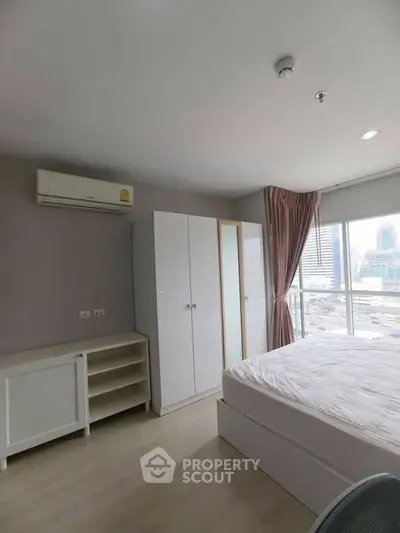 Modern bedroom with city view, featuring a comfortable bed, wardrobe, and air conditioning.
