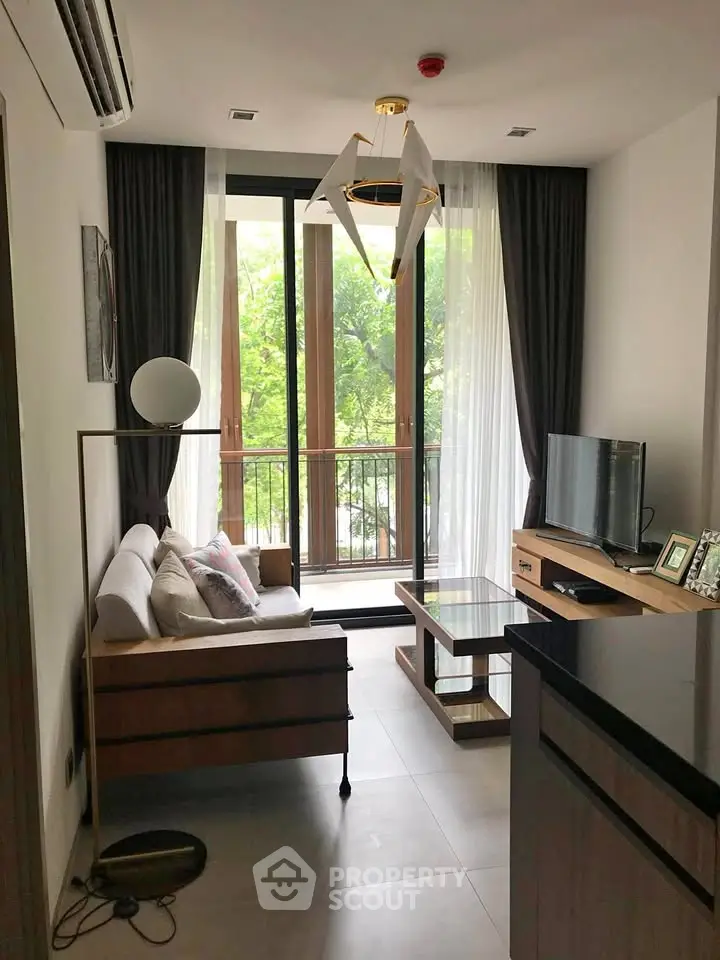Modern living room with large windows and stylish decor, offering a serene view of lush greenery.
