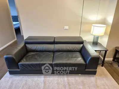 Modern living room with sleek black leather sofa and stylish lamp on side table.