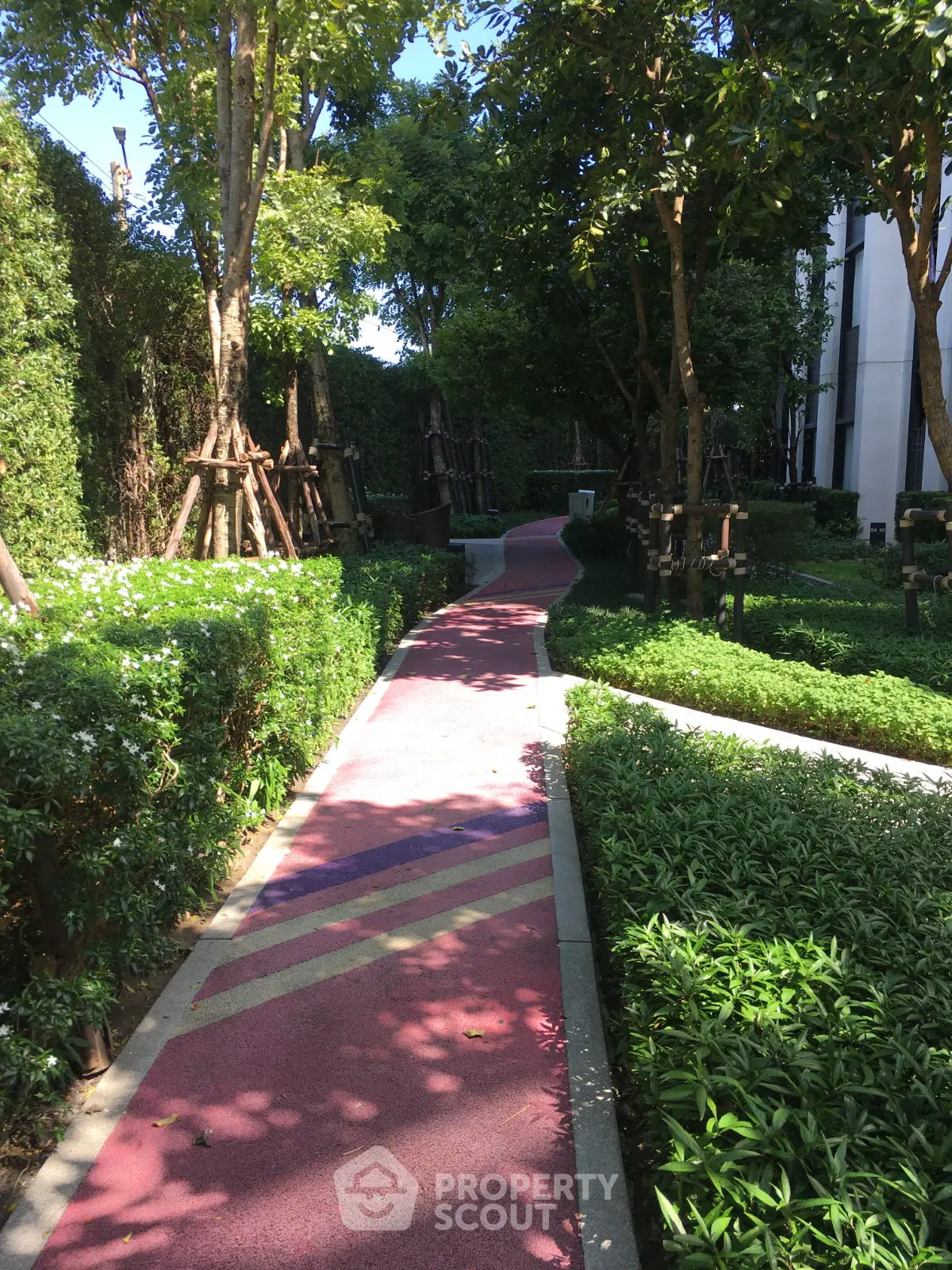 Lush garden pathway in modern residential complex with vibrant greenery and trees.