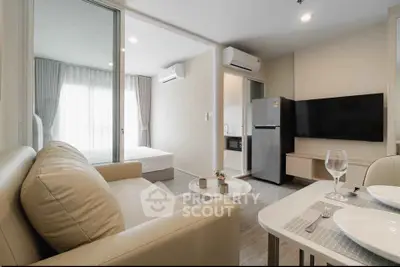 Modern open-plan living room with kitchen and bedroom, featuring sleek furniture and natural light.