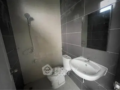 Modern bathroom with sleek gray tiles, wall-mounted shower, and contemporary fixtures.