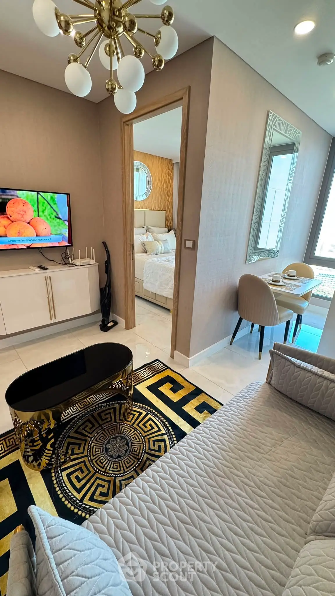Luxurious living room with elegant decor and stylish furniture, featuring a modern chandelier and a glimpse into a cozy bedroom.