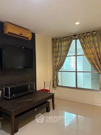 Cozy living room with modern TV setup and large window for natural light.