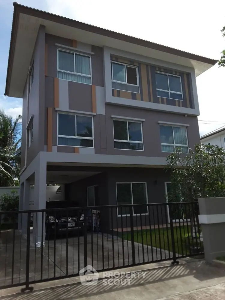 Modern three-story residential building with gated driveway and contemporary facade.
