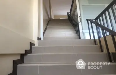 Pristine staircase in a modern residence with sleek metal railings and neutral-toned tiles, leading to a well-lit upper level.