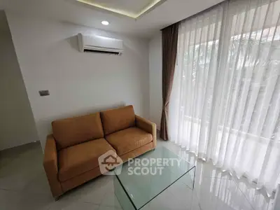Modern living room with cozy sofa and glass coffee table, featuring large window with sheer curtains.