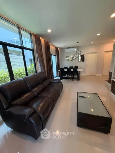 Spacious modern living room with leather sofa and dining area, featuring large windows and elegant decor.