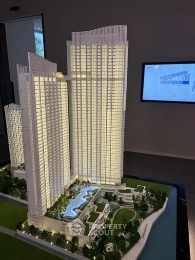 Architectural model of a modern high-rise residential complex with illuminated windows, showcasing a detailed miniature of the building's exterior and landscaped surroundings.