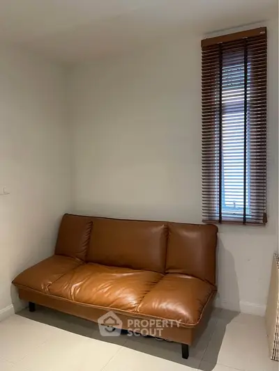 Cozy corner with a stylish brown leather sofa and window blinds, perfect for relaxation.