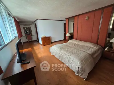 Spacious bedroom with wooden flooring and large windows for natural light.