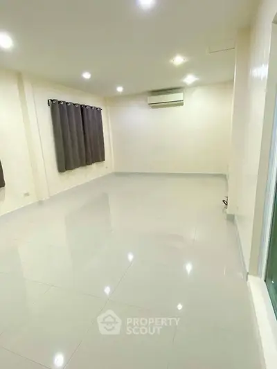 Spacious empty room with glossy tiled floor and air conditioning unit.