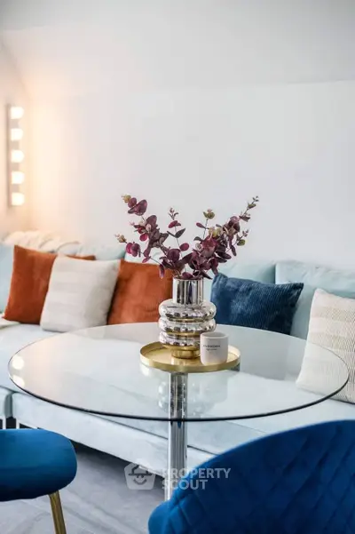 Stylish living room with modern decor and glass table, featuring colorful cushions and elegant lighting.