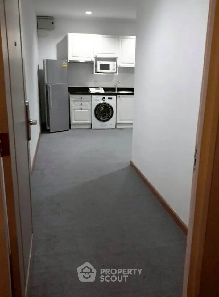 Compact kitchen with modern appliances including fridge, microwave, and washing machine in a cozy apartment.