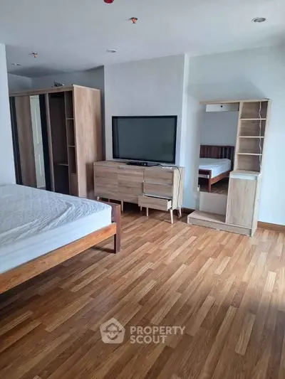 Spacious bedroom with modern wooden furniture and large TV, perfect for relaxation.