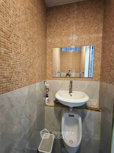 Compact bathroom with wall-mounted sink and urinal, featuring stylish tile design.