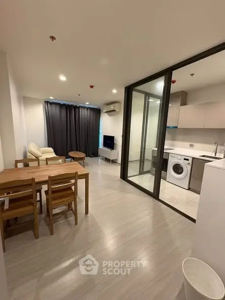 Modern open-plan living room with dining area and kitchen featuring a washing machine and sleek design.