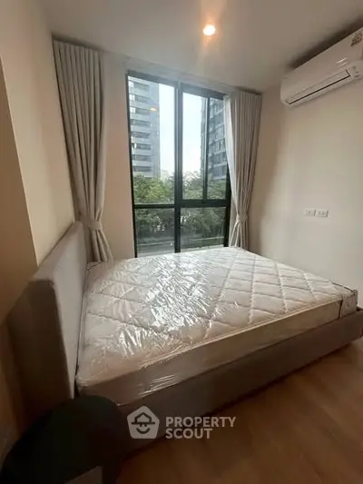 Modern bedroom with large window and city view, featuring a comfortable bed and air conditioning.