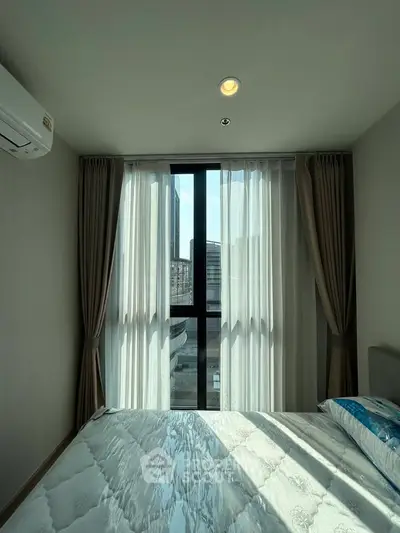 Bright bedroom with large window and city view, featuring modern decor and natural light.
