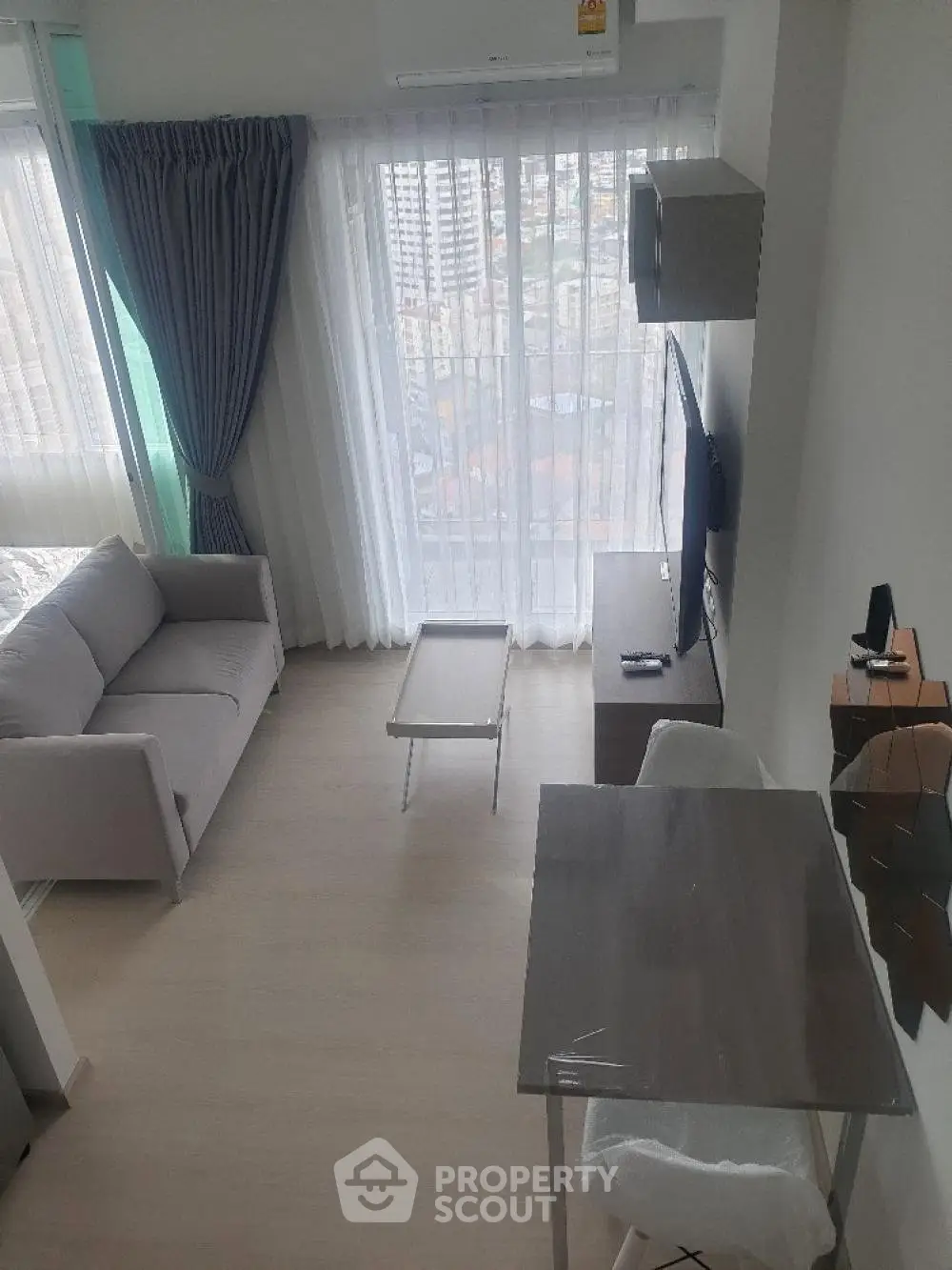 Modern living room with city view, featuring a cozy sofa, TV, and dining area in a high-rise apartment.