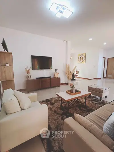 Spacious modern living room with stylish furniture and wall-mounted TV, perfect for relaxation and entertainment.