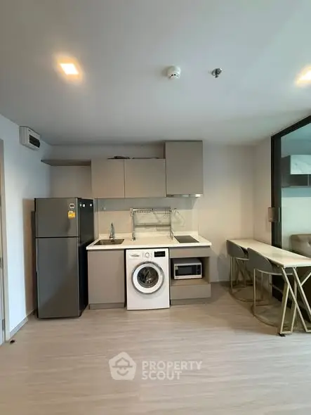 Modern kitchen with washing machine, fridge, and dining area in a compact apartment.