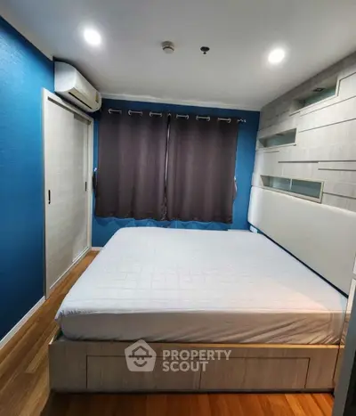 Modern bedroom with blue accent wall, wooden flooring, and built-in storage.