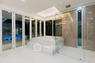 Luxurious modern bathroom with glass shower and large bathtub overlooking pool area.